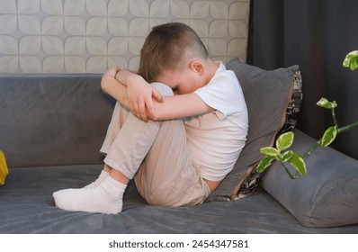 One sad little boy sitting in despair, alone at home on the sofa. Anxiety and stress. Concept of bullying, depressive stress or disappointment, sadness. Child abuse. - Powered by Shutterstock