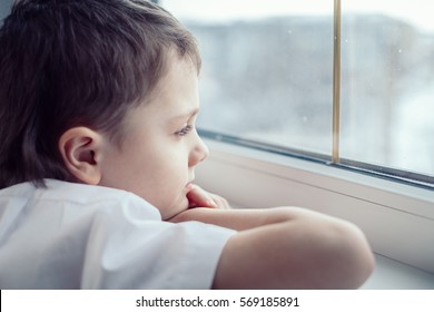 one sad little boy sitting near the window at the day time. Concept of sorrow.