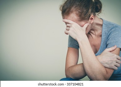 one sad woman sitting near a wall and holding her head in her hands