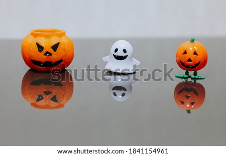 One scary orange pumpkin shaped candle, plastic white ghost toy and orange funny smiling pumpkin toy with green legs, isolated on grey background, space for text. Tradition Happy Halloween decoration.