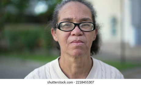 One Senior Hispanic Woman With Serious Expression Standing Outdoors Looking At Camera. Portrait Face Of An Older South American Lady