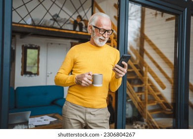 One senior man with a beard stand on the balcony hold a mobile phone and cup of coffee happy smile daily morning routine real person copy space read or use smartphone internet browse social network - Powered by Shutterstock