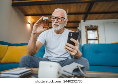 One senior man sitting at home on sofa bed holding bottle of medicine pills medicament or supplement and smartphone read label instructions of drug tablet painkillers or vitamin ready to take medicine - Powered by Shutterstock