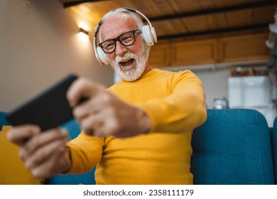 One senior old caucasian man sit at home happy smile play video games leisure activity having fun hold mobile phone smartphone have fun copy space - Shutterstock ID 2358111179
