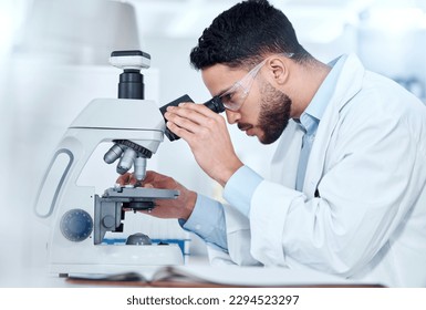 One serious medical scientist sitting at a desk and using a microscope to examine and analyse test samples on slides. Hispanic healthcare professional discovering a cure for diseases in his laboratory