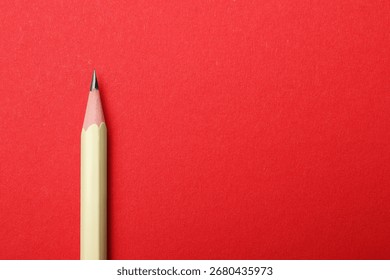 One sharp graphite pencil on red background, top view. Space for text