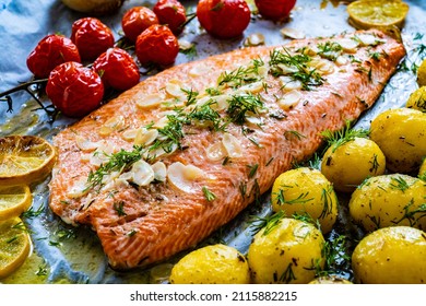  One sheet pan roast trout fillet with potatoes and vegetable salad served on black stone plate on wooden table 