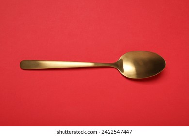 One shiny golden spoon on red background, top view