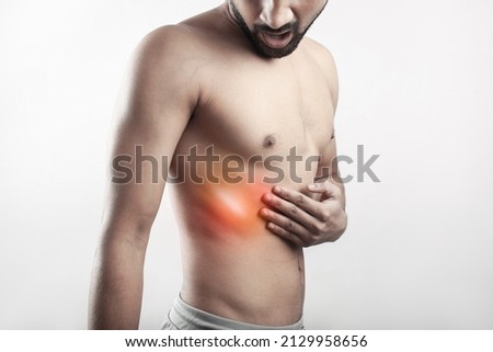 One shirtless male with painful grimace expression on face touching his thoracic cage with pain highlighted in glowing red.