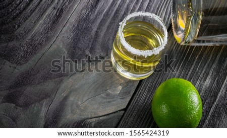 one shot of tequila with a bottle lying on a dark wooden background. the tradition of drinking strong alcohol.
