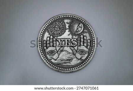 One side of an antique silver divinity coin, writing saying "YES".