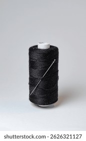 One single black thread spool with needle on white background