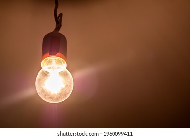 One single old plain bright incandescent lightbulb on in a darkened room, object detail, closeup, from below Bright yellow light source illuminates the room, light in the dark abstract concept, nobody