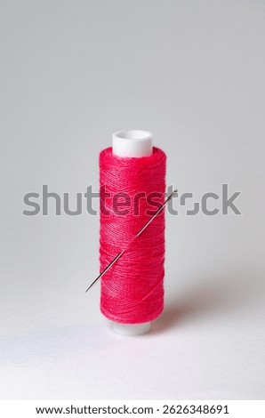 One single pink thread spool with needle on white background