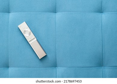 One Single Simple Sliver Smart TV Remote Control Laying On A Blue Sofa Pillow At Home, Object Top View, Closeup, Nobody. Leisure, Rest, Watching TV Symbol, Concept, Copy Space Background, No People