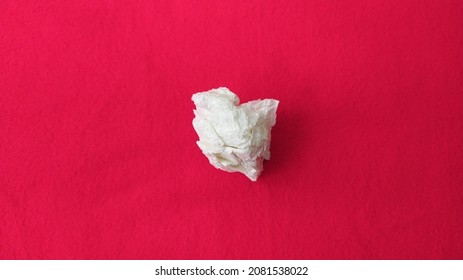 One Single Twisted Used Dirty Leftover White Tissue Paper Or Napkin Scattered And Isolated On Red Restaurant Table Cloth Background Texture With Copy Space. Horizontal Closeup Macro Flat Lay Top View