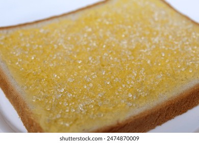 One slice of white square bread, with margarine spread and white crystal sugar topping, isolated on white background