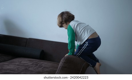 One small boy climbs on sofa edge playing at home. Child mounting on top of couch - Powered by Shutterstock