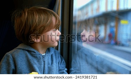 One small boy traveling by train leaning on glass staring at view, reflection of child's face on window