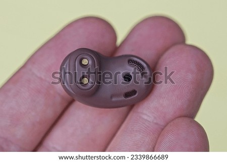 one small brown plastic wireless headphone lies on the fingers on the hand on a yellow background