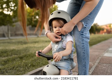 One Small Caucasian Girl Or Boy Mother Young Woman Adjust Protective Helmet Putting On Child Daughter While Playing With Kick Scooter Outdoor In Summer Day Leisure Family Growing Up Childhood Concept