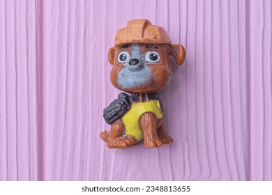 one small colored plastic old dirty toy dog lies on a pink wooden table