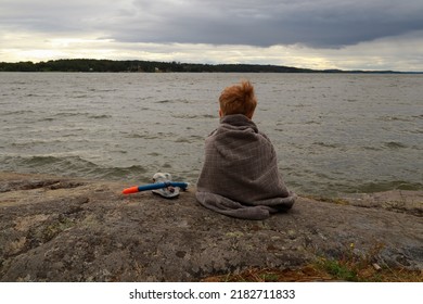 One Small Kid At A Lake. Cold Summer Weather One Cloudy Day. Wrapped In A Large Towel. Backside Towards Camera. Waiting For The Sun. Mälaren, Stockholm, Sweden, Scandinavia, Europe.