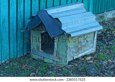 one small old wooden makeshift close green color  doghouse  empty handmade with iron roof warm dog-free booth stands on the ground near a green wooden fence on the street 
