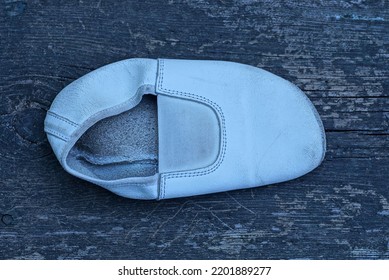 One Small White Leather Old Slipper Stands On A Gray Wooden Table