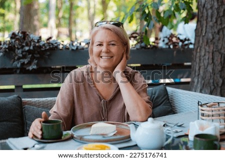 One smiling elegant well-groomed elderly senior woman cup of tea or coffee drink summer cafe breakfast. Lifestyle and recreation of a retired tourist in the city. 50-60 years old age