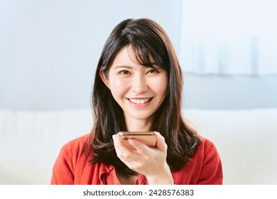 One smiling woman in her 30s in her 30s looking for a smartphone in front of her mouth and using the technique of audio recognition in front of her mouth