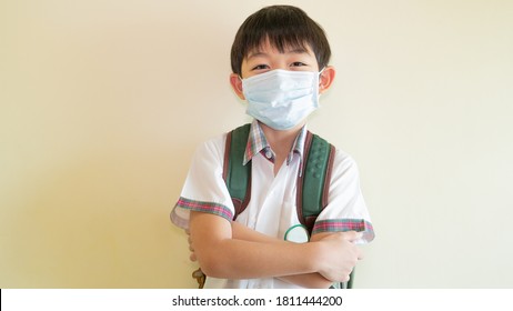 One Smiling Young Student Is Wearing The Surgical Mask And Crossing His Arms. Asian Kid Is Ready For The School During COVID 19 Concept.