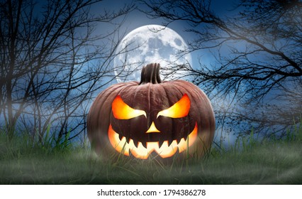 One spooky halloween pumpkin, Jack O Lantern, with an evil face and eyes on the grass with a misty night sky background with a full moon.