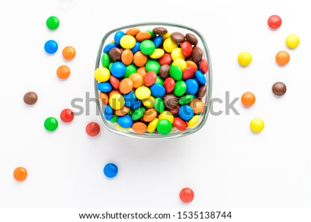 One squared bowl with small  red, yellow, green, blue, brown and orange coated chocolate candies isolated on white background, top view
