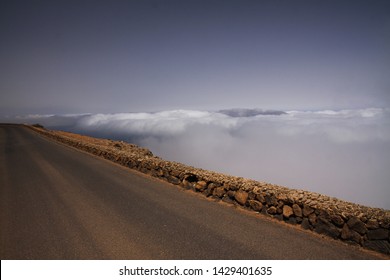 One Step Away From The Abyss: Scenic Road On High Mountain Peak Viewpoint Above Clouds With Natural Stone Wall Close To Abyss (Mirador Del Rio - Lanzarote)