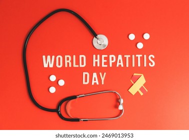 One stethoscope, white pills, a yellow-red ribbon and light wooden letters with the lined phrase World Hepatitis Day lie in the center on a red background, flat lay close-up. - Powered by Shutterstock