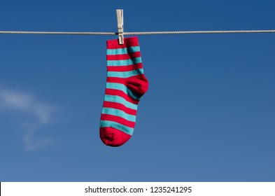 One Strip Sock And White Clothespin On A Blue Sky Background