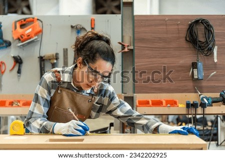 One Strong confident young aged women carpenter standing aim at wood plank in workshop. Latin female carpenter entrepreneur working craft with wood diy tool in workbench shop carpentry