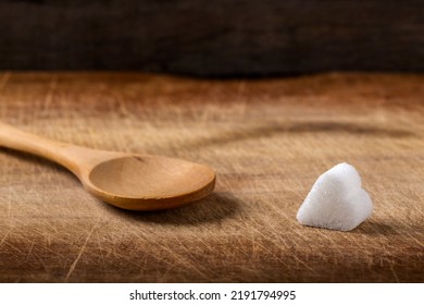 One Sugar Cube - Heart Shape - And One Empty Wooden Spoon In Background