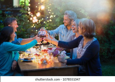 Eines Sommerabends versammelten sich Freunde in ihren vierziger Jahren um einen Tisch im Garten, der von leuchtenden Gartenlandschaften beleuchtet wird. Sie toast mit ihrer Weinbrille