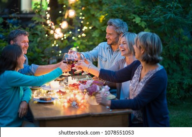 One summer evening, friends in their forties gathered around a table in the garden lit by luminous garlands. They toast with their glasses of wine - Powered by Shutterstock