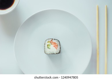 One Sushi Roll on white plate with chopsticks. Roll made of Fresh Raw Salmon, Cream Cheese and cucumber. Isolated on white background. Japanese seafood sushi roll on a white background.