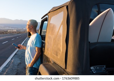 one teenager alone in the street with his car at sunset using his phone and looking at the sun in his vacations outdoors concept and lifestyle - Powered by Shutterstock