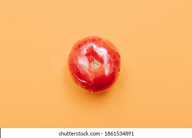 One Tomato In Wrap Polyethylene Plastic On Orange Background. Minimal Enviromental Concept. Flat Flat, Top View