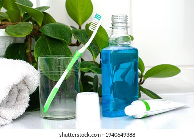 One Toothbrushe In A Glass Cup Mouthwash A Tube Of Toothpaste And A Rolled Up Towel On The Dressing Table Against A Backdrop Of Green Foliage. High Quality Photo