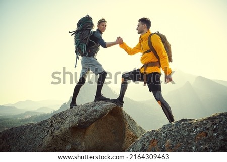 One tourist climber helps another, standing on top of a mountain. Friendship and mutual assistance. Extreme sports, mountain tourism.