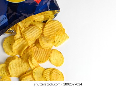 One Of The Types Of Snacks, Fast Food, Junk Food - Ruffled Potato Chips Spilling Out Of An Open Bag On A White Background  