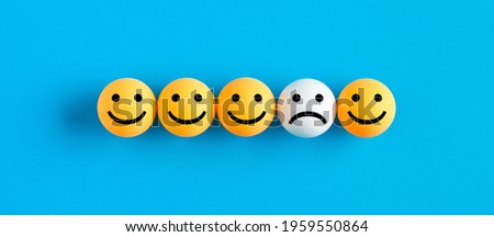 One unhappy face emoticon among happy face emojis in a row. Customer dissatisfaction or unhappy client concept.