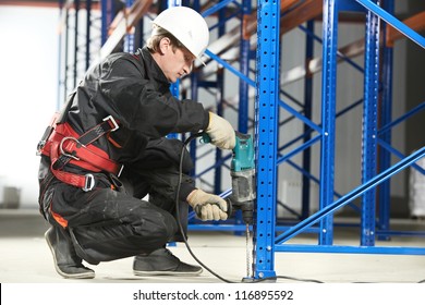 One warehouse worker in uniform with power tool drilling hole during rack arrangement erection work