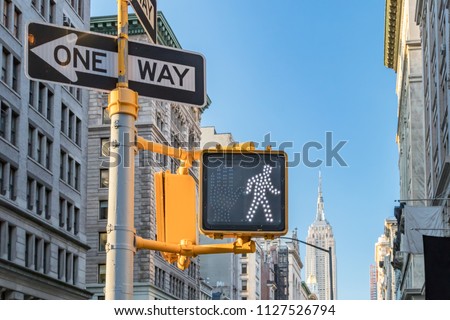 One way and crosswalk signs on a street in Manhattan with the New York City skyline in the background